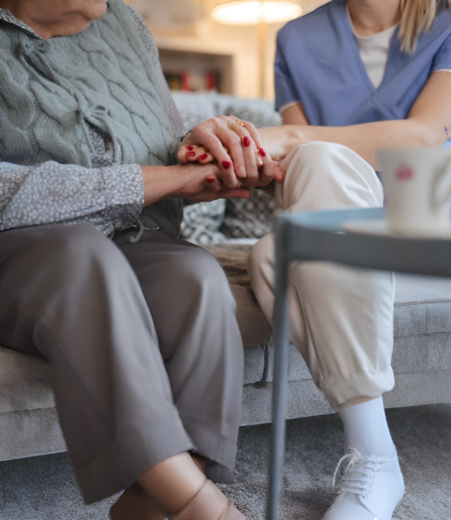 Alegria caregiver sitting with an elderly client at home, holding her hands